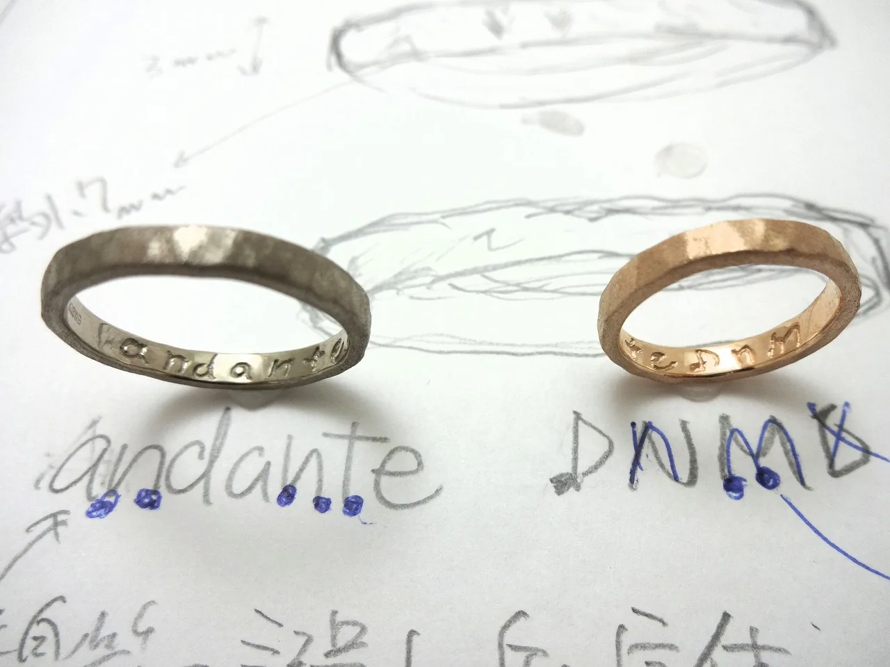 ふたりで描いたデザイン画の上に置かれた手作り結婚指輪のペア