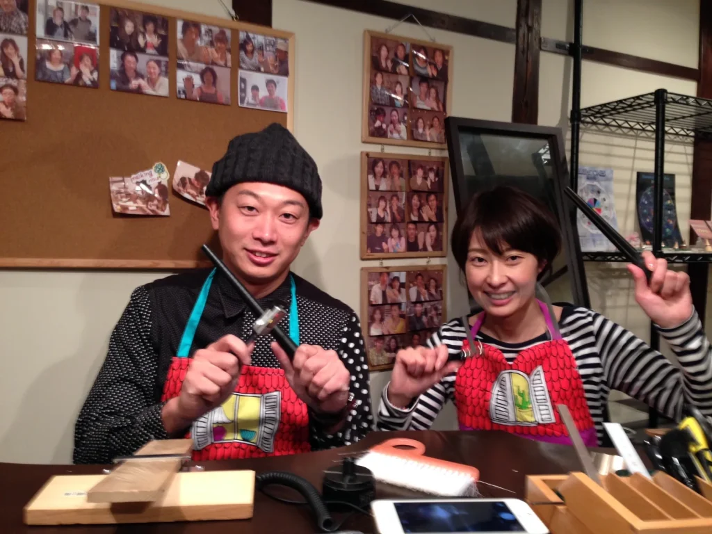 手作り結婚指輪の制作体験中、金槌などの工具を手に笑顔を見せるカップル。工房でふたりが指輪づくりを楽しむ様子