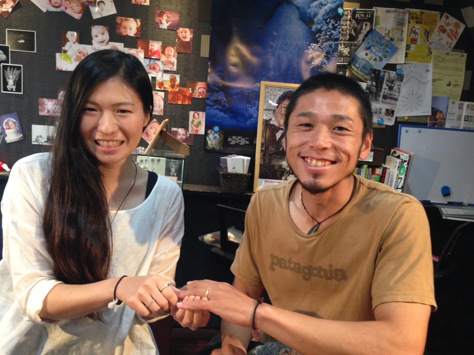 手作り結婚指輪が完成し、指輪をのせた手を差し出して笑顔を見せるカップル。工房のカウンターで受け取った、ふたりだけのペアリングの記念写真