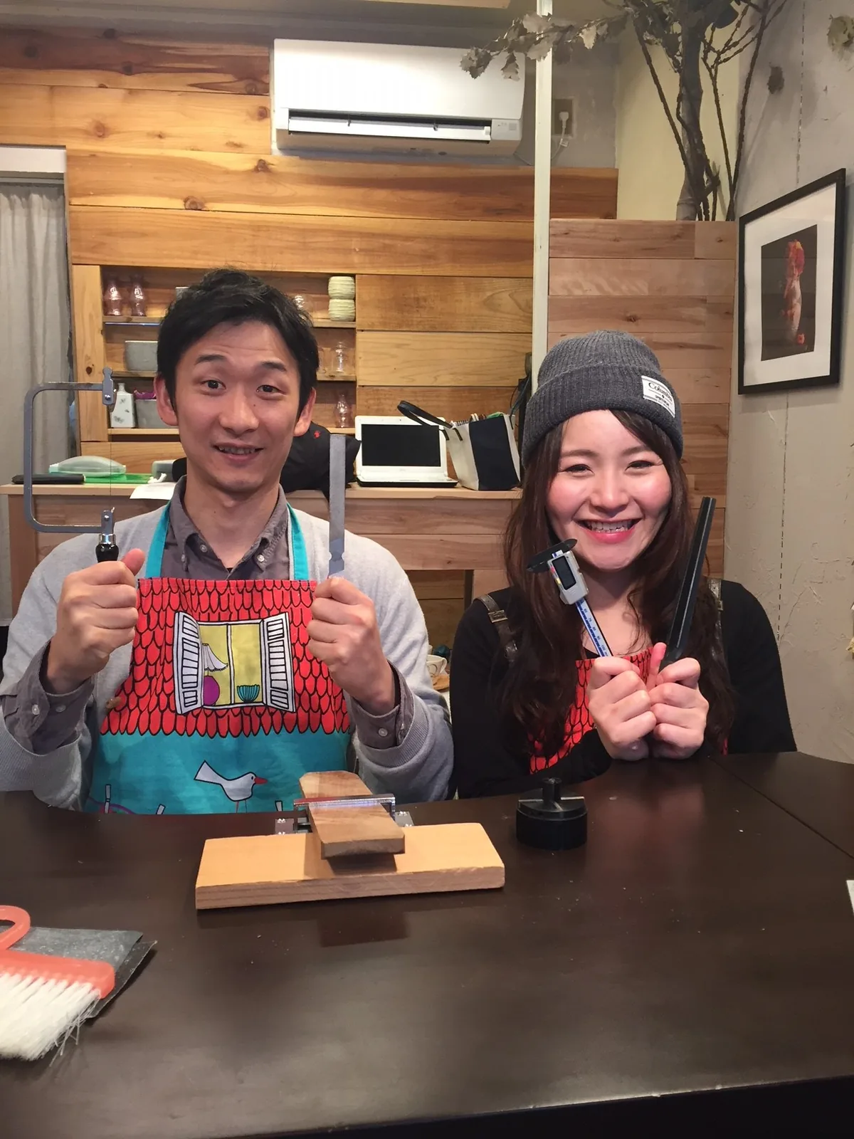 手作り結婚指輪の工房で、ノギスなどの道具を持ち大きな笑顔を見せるカップル。ふたりで制作体験を楽しむ温かで賑やかな雰囲気