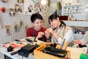 明るく温かい工房で、緑のワックス原型を二人で確かめ合う笑顔のカップル。手作り結婚指輪の制作体験の様子