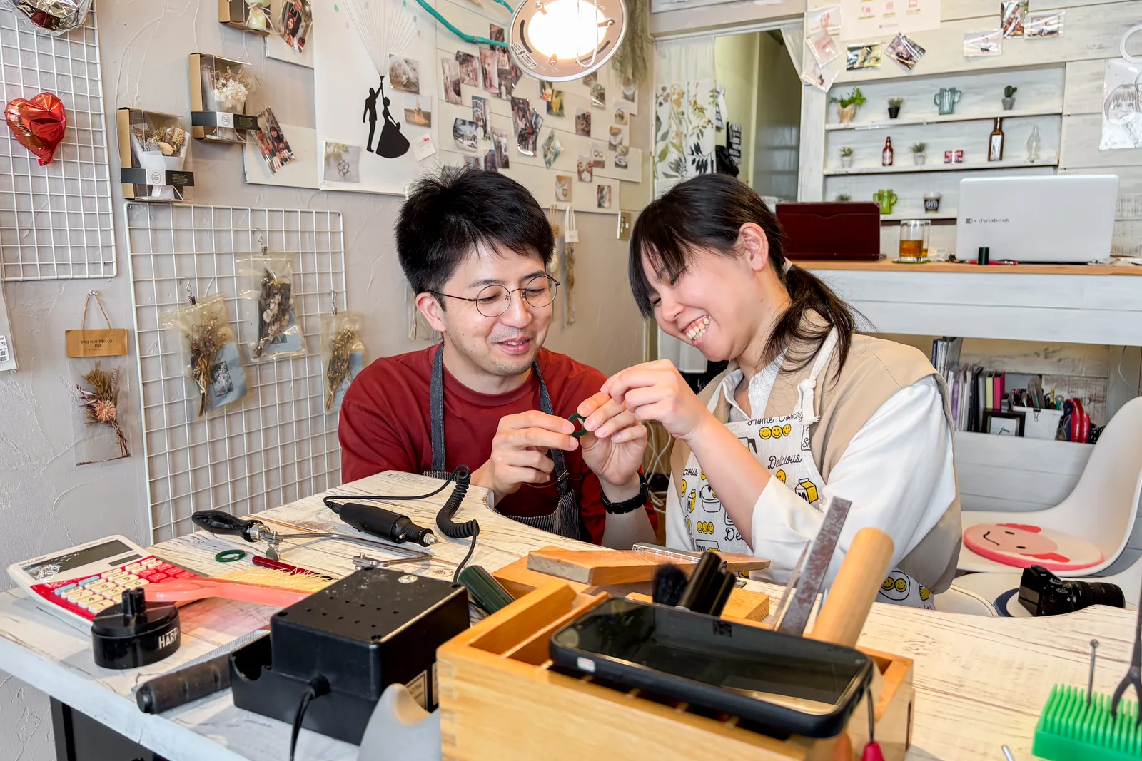 明るく温かい工房で、緑のワックス原型を二人で確かめ合う笑顔のカップル。手作り結婚指輪の制作体験の様子