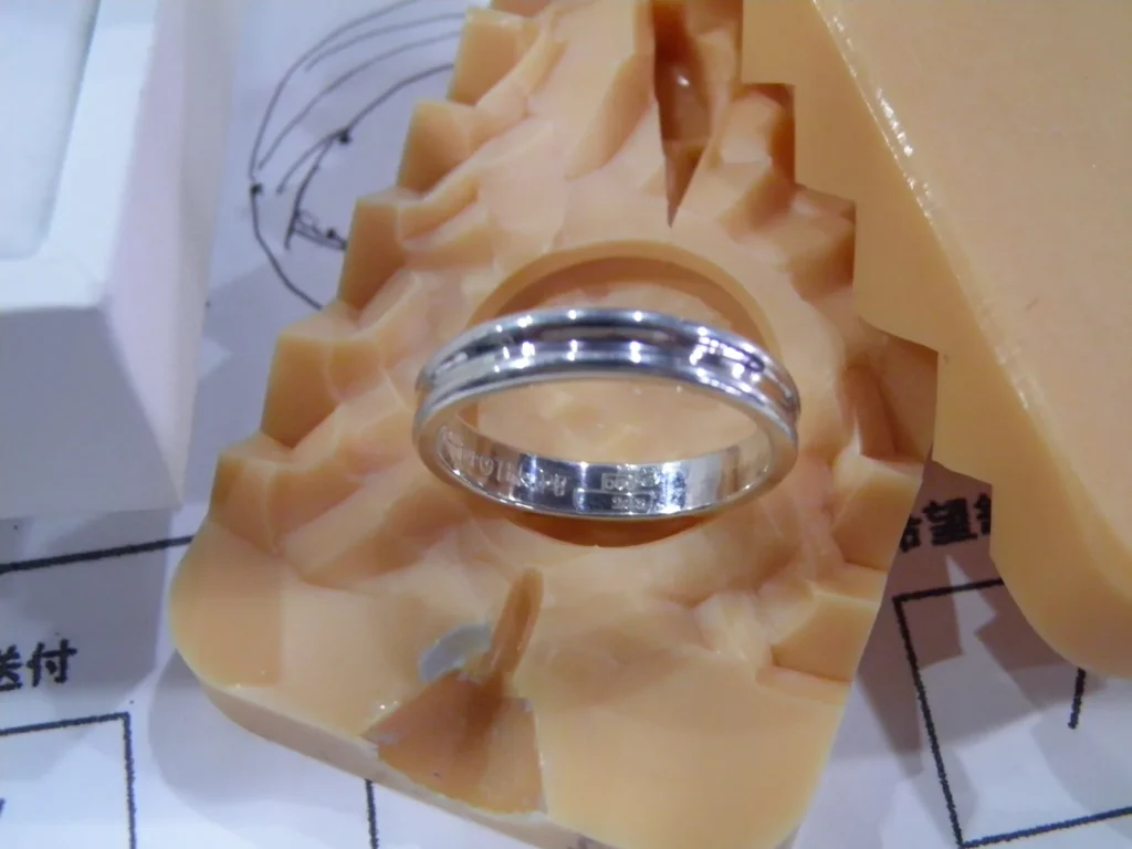 削り出したワックス原型の上に置かれた完成間近のプラチナ結婚指輪。内側の刻印も見える、手作り結婚指輪の制作工程を伝える一枚